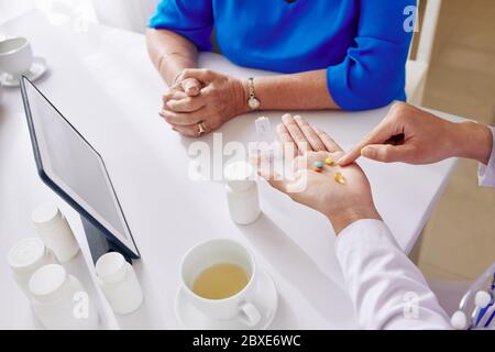Doktor zeigt auf Pillen in der Hand, wenn sie erklärt, ältere Frau hay viele Ergänzungen sie täglich nehmen sollte Stockfoto