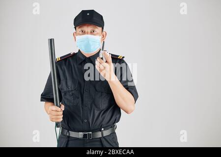 Porträt des Sicherheitsbeamten in medizinischen Maske halten Knüppel und sprechen auf Walkie-Talkie Stockfoto