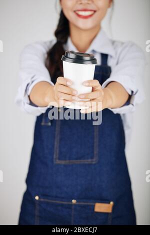Nahaufnahme des jungen weiblichen Barista in Denim-Schürze, die eine Tasse leckeren Kaffee zum Mitnehmen gibt Stockfoto