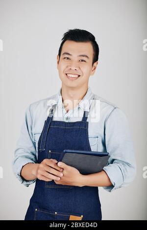 Positiv schöner junger Cafe Kellner mit digitalem Tablet vor grauem Hintergrund Stockfoto