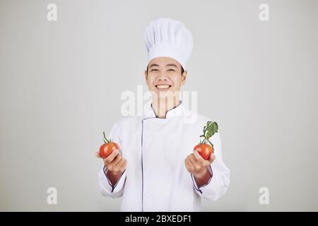 Porträt von glücklichen schönen jungen Koch in Uniform hält frische reife Tomaten Stockfoto