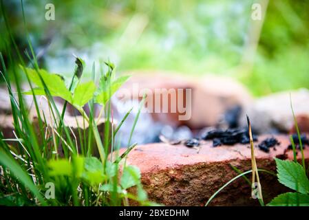 Die Glut eines toten Feuers ist Rauchen im Ziegelzaun. Das Feuer nach dem Grill. Stockfoto