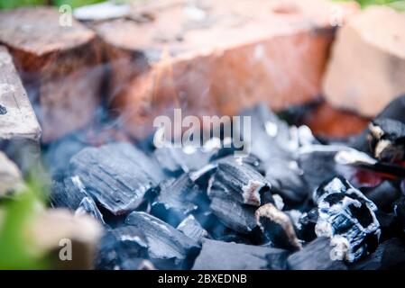 Die Glut eines toten Feuers ist Rauchen im Ziegelzaun. Das Feuer nach dem Grill. Stockfoto