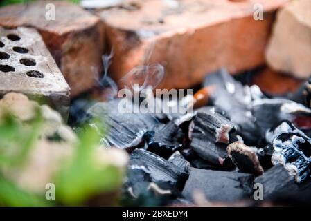 Die Glut eines toten Feuers ist Rauchen im Ziegelzaun. Das Feuer nach dem Grill. Stockfoto