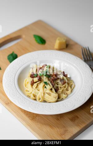 Traditionelle italienische Pasta Fettuccine Alfredo mit sonnengetrockneten Tomaten und Basilikum vegan. Sauce aus Bechamel, Milch auf pflanzlicher Basis, Olivenöl Stockfoto