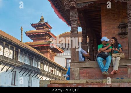 Ein junges nepalesisches Paar hat einen romantischen, sanften Moment gefangen, während es im Schatten eines Tempels auf dem Durbar Square, Kathmandu, Nepal saß Stockfoto