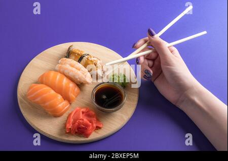 Nahaufnahme des Sashimi Sushi-Sets auf Holzplatte, weibliche Hand mit Essstäbchen. Leckere japanische Meeresfrüchte, Restaurantkonzept Stockfoto