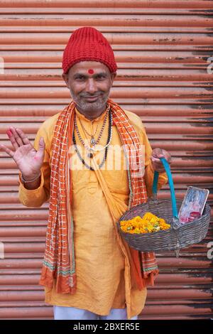 Ein hinduistischer Priester in Kathmandu, Nepal, der mit einem Blumenkorb von Geschäft zu Geschäft oder von Haus zu Haus geht, segnende Ladenbesitzer und andere Laien Stockfoto