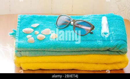 Desinfektionsflasche, Sonnenbrille und Muscheln liegen auf einem blauen Handtuch. Das Konzept eines Sommerurlaubs in einer neuen Realität. Stockfoto