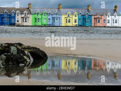 Mehrfarbige Häuser mit Blick auf den Strand von Borth mit einem Vordergrund von Unkraut bedeckt Felsen und Reflexionen der Häuser in einem Pool aus nassem Sand Stockfoto