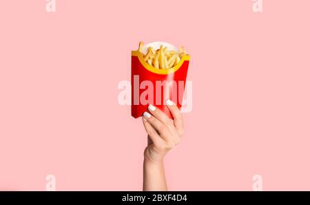 KHARKIV, UKRAINE - 4. APRIL 2020: Weibliche Hand zeigt pommes von McDonald's in roter Verpackung auf farbigem Hintergrund Stockfoto