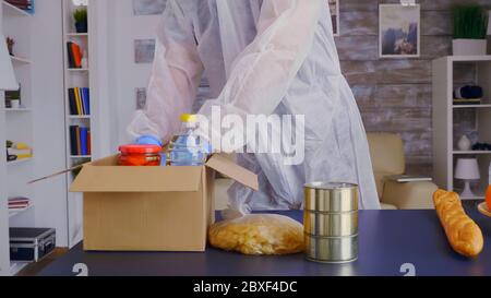 Nahaufnahme eines Freiwilligen mit Handschuhen, die Lebensmittel mit Schutzanzug gegen Coronavirus verpacken. Stockfoto