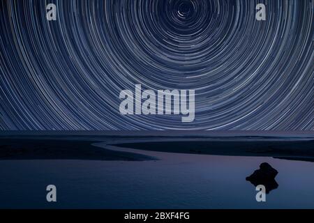 Digitales Verbundbild von Sternspuren rund um Polaris mit Landschaft von Ebbe Strand Stockfoto