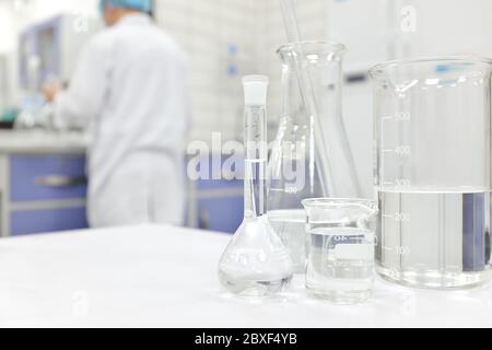 Blur-Wissenschaftler, der in einem Chemistry Science-Labor mit Kolben, Becher und Glaswaren arbeitet, die klare flüssige Chemikalien enthalten. Stockfoto