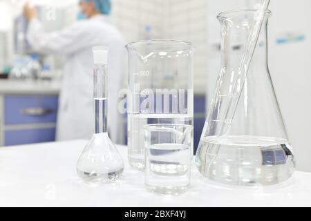 Blur-Wissenschaftler, der in einem Chemistry Science-Labor mit Kolben, Becher und Glaswaren arbeitet, die klare flüssige Chemikalien enthalten. Stockfoto