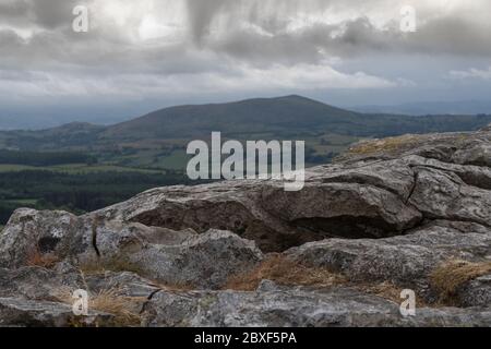 Ein walisischer Berg, der von einem Felsen in den Shropshire Hills mit dunklen Wolken betrachtet wird Stockfoto