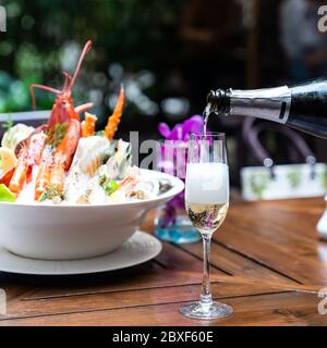 Kellner gießt Weißwein in Weinglas und serviert dem Kunden im Restaurant mit großer Schüssel Meeresfrüchte auf Eis im Hintergrund. Restaurant Gastronomie Essen Stockfoto