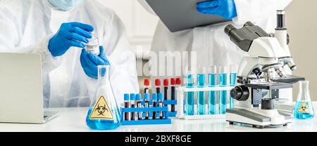 Wissenschaftler halten Impfstoff gegen das immune Coronavirus COVID-19 Pandemie im Wissenschaftslabor. Sie tragen persönliche Schutzanzüge und Handschuhe. Medizinisch Stockfoto