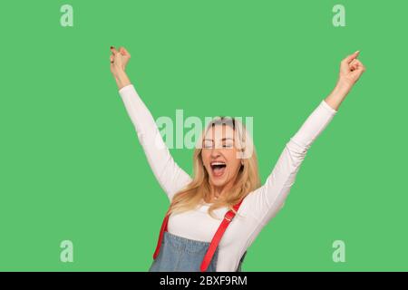 Ja, ich bin Gewinner! Porträt von begeisterten erwachsenen Frau in stilvollen Denim Overalls schreien Hurra und halten die Hände hoch, Freude Sieg, Ziel erreicht Stockfoto