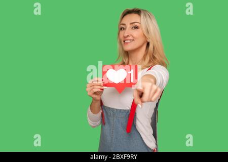 Sie drücken wie und folgen Social Media Blog! Porträt von schönen fröhlichen erwachsenen Frau mit Netzwerk Herz-Symbol und zeigt auf Kamera, zeigt Emoji b Stockfoto