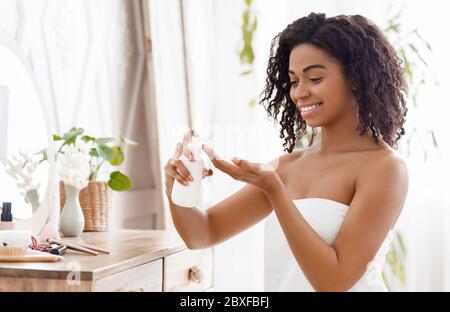 Feuchtigkeitsspendende Haut. Lächelnde Afrikanische Frau Anwendung Body Lotion Im Schlafzimmer Zu Hause Stockfoto