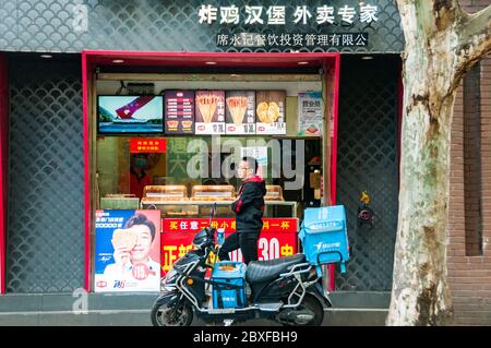 Ein Lieferer wartet auf eine Bestellung vor einem Brathähnchenladen in der Jiaozhou Road in Shanghai. Stockfoto