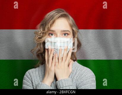 Panikartige Frau mit Gesichtsmaske auf Ungarn Flagge Hintergrund. Konzept für Grippeepidemie und Virenschutz Stockfoto