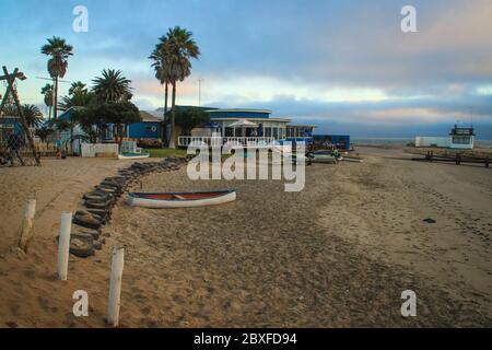 Walvis Bay, Namibia - 25. April 2015: Atlantikküste. Leerer Strand mit Boot, Palmen und Restaurants bei Sonnenuntergang. Stockfoto