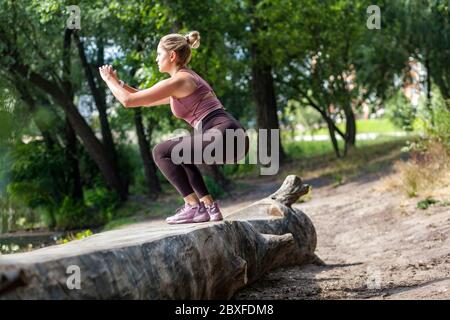 Persönliches Workout-Programm. Sportliche sportliche Frau im Trainingsanzug hocken tun Sit-ups im Wald im Freien, Training allein Aufwärmen vor dem Joggen, Exer Stockfoto