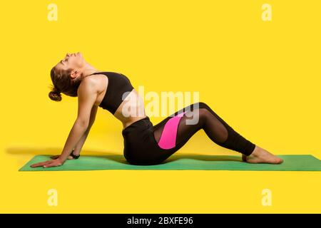 Fitness Frau mit Haar-Bun in engen Sportbekleidung sitzt auf Turnhalle Matte Sport zu tun, nach hinten Dehnen Rückenmuskeln, Aufwärmen mit flexibili Stockfoto