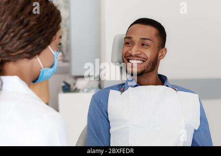 Junger schwarzer Mann lächelt zu Zahnärztin Stockfoto