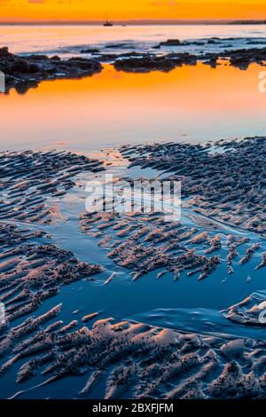 Wellen und Reflexionen auf nassem Strandsand im frühen Morgenlicht Stockfoto