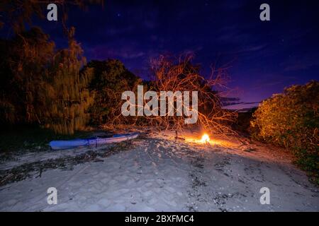 Kajak liegt am Sandstrand in der Nähe Lagerfeuer in der Nacht Stockfoto