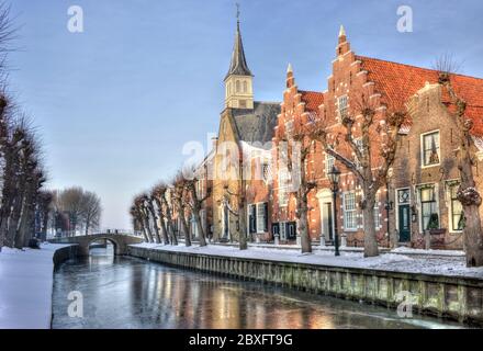 Malerischer Winterblick auf eine Reihe historischer Häuser und Kirche mit einer kleinen Brücke im malerischen Dorf Sloten in den Niederlanden Stockfoto