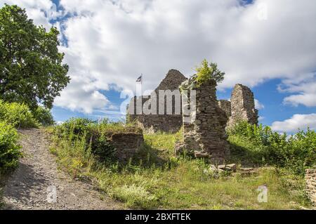 Weg zu den Ruinen einer mittelalterlichen Burg, die an einem leicht bewölkten Sommertag von der Sonne beleuchtet wird. Flagge oben. Stockfoto