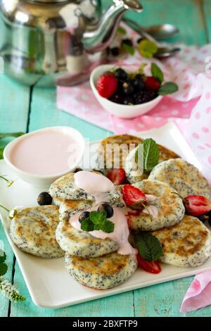 Sommerfrühstück. Hausgemachte Quark-Pfannkuchen mit Mohn, saure Sahne-Sauce mit Erdbeeren. Stockfoto
