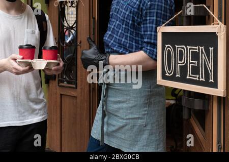 Die Hände des Kellners halten zwei Tassen Kaffee in der Nähe der Tür des Cafés. Arbeiter gibt einen Auftrag zum Mitnehmen für Kunden des Straßenmarktes. Stockfoto