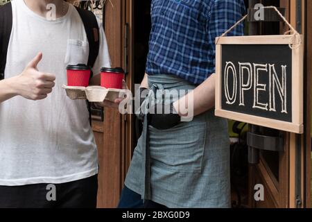 Die Hände des Kellners halten zwei Tassen Kaffee in der Nähe der Tür des Cafés. Arbeiter gibt einen Auftrag zum Mitnehmen für Kunden des Straßenmarktes. Stockfoto