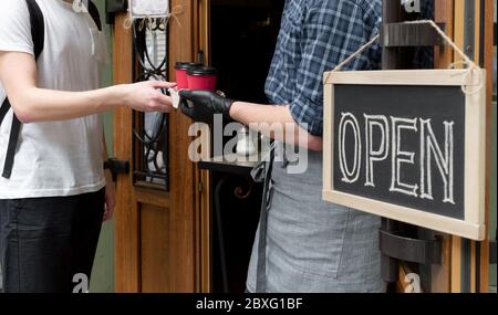 Die Hände des Kellners halten zwei Tassen Kaffee in der Nähe der Tür des Cafés. Arbeiter gibt einen Auftrag zum Mitnehmen für Kunden des Straßenmarktes. Stockfoto