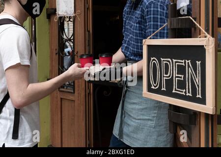 Die Hände des Kellners halten zwei Tassen Kaffee in der Nähe der Tür des Cafés. Arbeiter gibt einen Auftrag zum Mitnehmen für Kunden des Straßenmarktes. Stockfoto