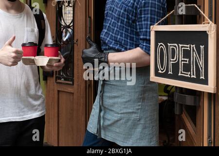 Die Hände des Kellners halten zwei Tassen Kaffee in der Nähe der Tür des Cafés. Arbeiter gibt einen Auftrag zum Mitnehmen für Kunden des Straßenmarktes. Stockfoto