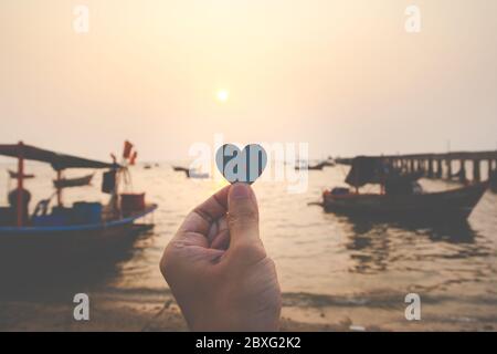 Nahaufnahme der Hand Mann hält ein Papier Herz mit dem Meer Hintergrund am Abend. Love Konzept, Happy valentine. Stockfoto