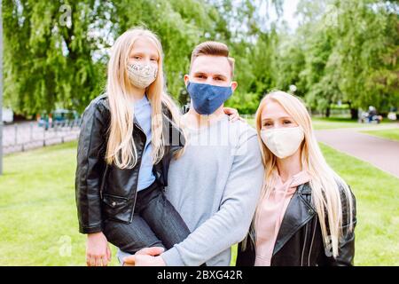 Familienmitglieder umarmen sich gegenseitig und lächeln in der Kamera mit Stoffmaske. Vater, Mutter und Tochter schützen sich vor dem Virus Stockfoto