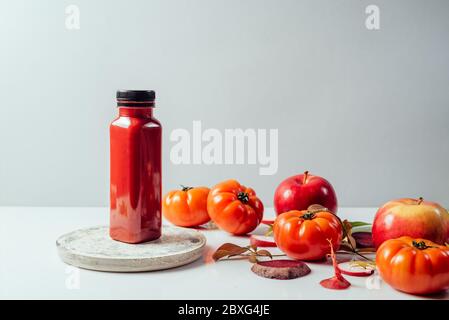 Roter Smoothie Getränk in der Flasche in der Nähe von reifen Äpfeln Tomaten und Rüben. Detox Diät für gesunden Körper und Geist. Gesundheit Ernährung Konzept. Vorderansicht auf grauer Rückseite Stockfoto