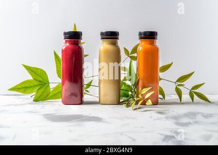 Rote, orange und gelbe Smoothies und Säfte Getränke in Flaschen mit verschiedenen frischen Bio-Früchten und Beeren Zutaten auf weißem Hintergrund Stockfoto