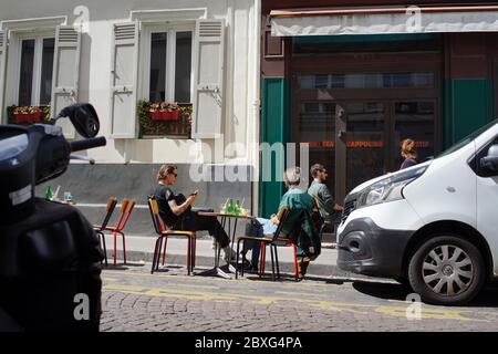 Menschen genießen einen Drink auf einer temporären Café-Terrasse, zwischen geparkten Autos, im Leben nach der Sperre - Rue Muller, Montmartre 75018 Paris, Frankreich Stockfoto