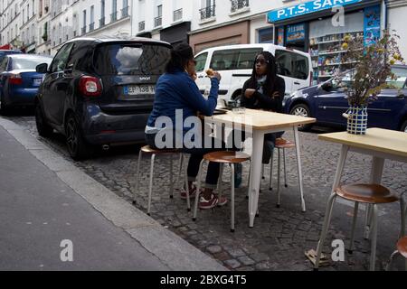 Pariser genießen eine temporäre Café-Terrasse, zwischen geparkten Autos im Leben nach der Sperre - Rue Muller, Montmartre 75018 Paris, Frankreich Stockfoto