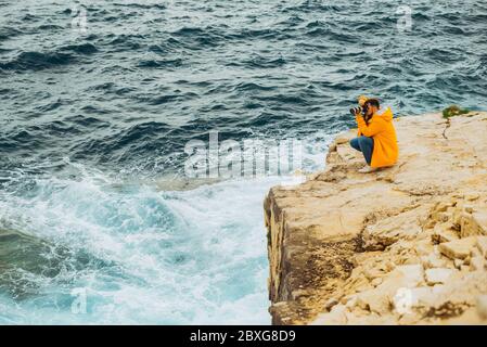Mann Fotograf, der auf der Kamera am Rand der Klippe steht Stockfoto