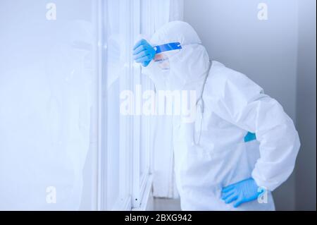 Müde Arzt mit PSA gegen ein Fenster lehnend, Thailand Stockfoto