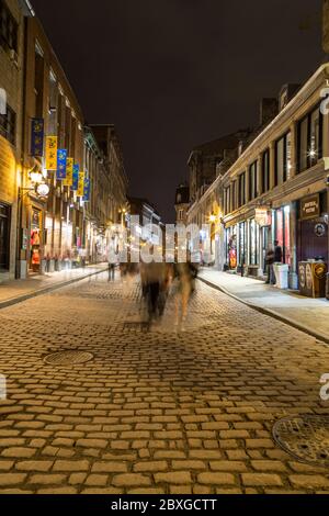 MONTREAL, KANADA - 17. MAI 2015: Gebäude und Geschäfte entlang der Rue Saint Paul in der Altstadt von Montreal bei Nacht. Die Unschärfe der Menschen ist zu sehen. Stockfoto